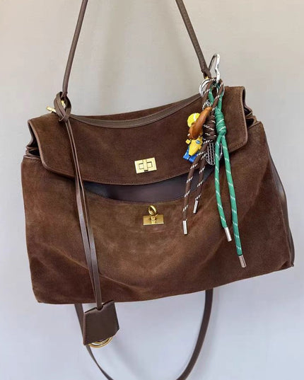 Brown suede handbag with decorative keychain on a light background