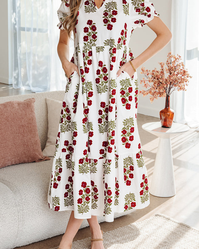 Woman wearing a white dress with red floral patterns in a living room setting.