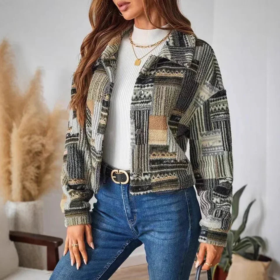 Woman wearing a patterned jacket and blue jeans indoors with decorative plants.
