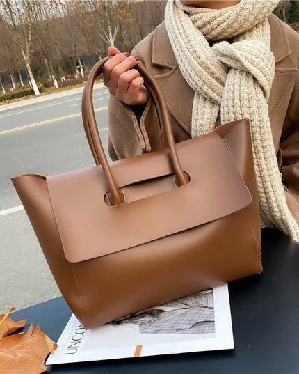 Person holding a brown handbag with a scarf, standing on a road.
