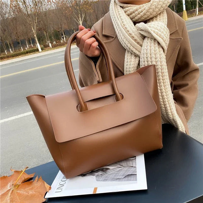 Person holding a brown handbag with a scarf, standing on a road.
