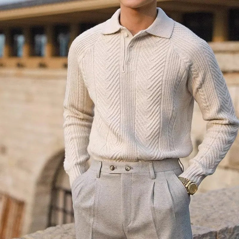 Man wearing a beige knitted sweater and light gray pants with a blurred background