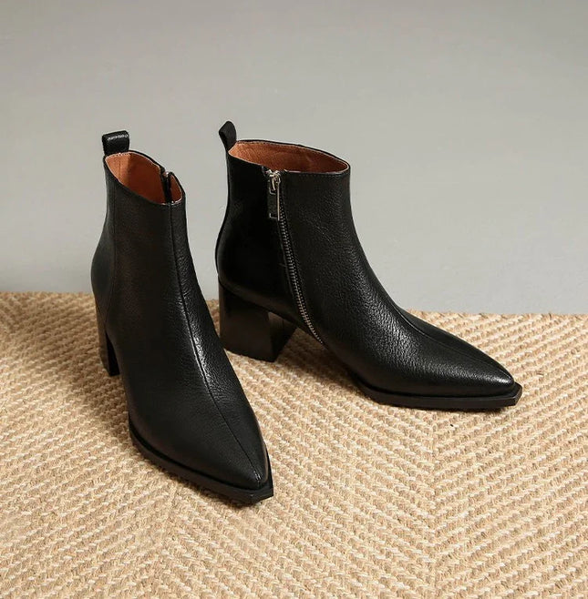 Pair of black leather ankle boots on a textured surface with a neutral background
