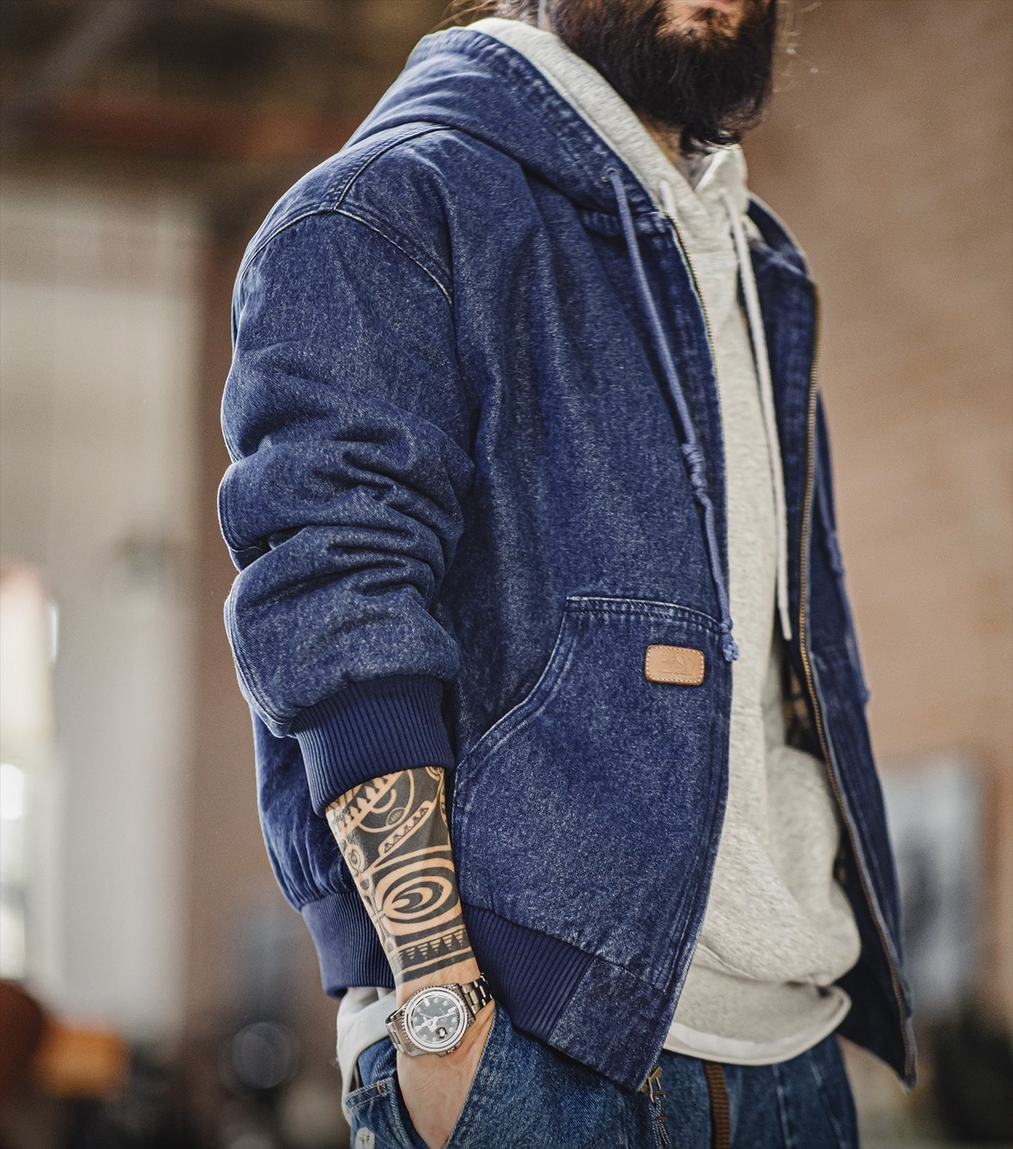 Person wearing a blue denim jacket with a visible brand logo, standing indoors.