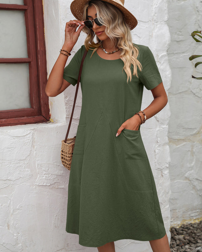 Woman wearing a green dress with a straw hat and sunglasses against a white wall.
