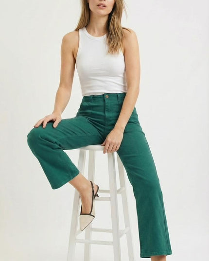 Woman sitting on a white stool wearing a white top and green pants against a white background