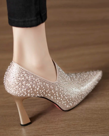 High-heeled shoe with pearl embellishments on a wooden floor