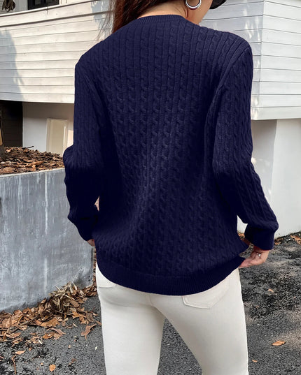 Person wearing a navy blue cable knit sweater and white pants standing outdoors.