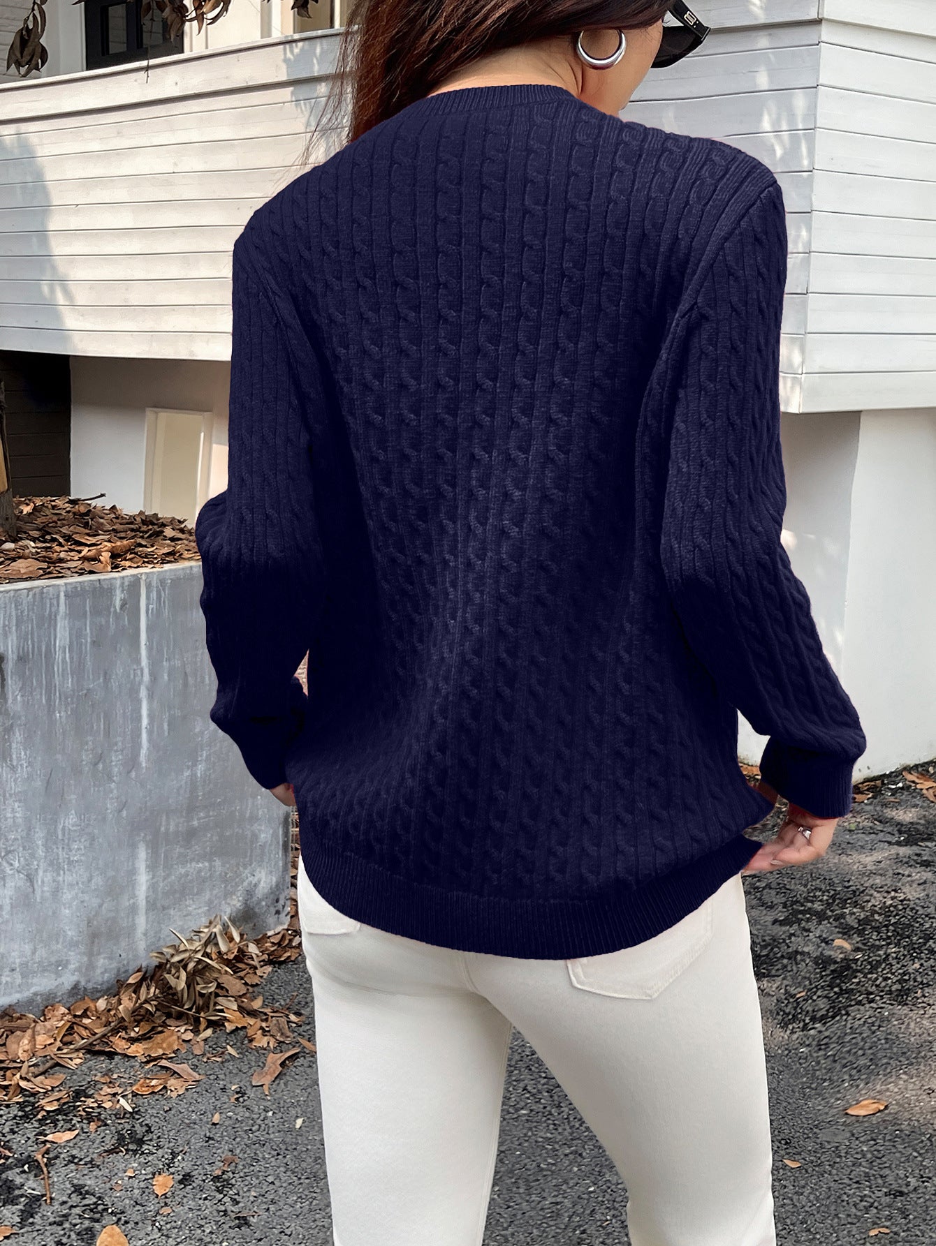 Person wearing a navy blue cable knit sweater and white pants standing outdoors.