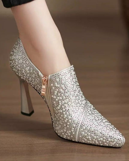 Silver stiletto heel shoe with rhinestone embellishments on a wooden floor.