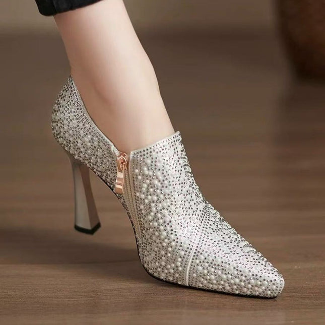 Silver stiletto heel shoe with rhinestone embellishments on a wooden floor.