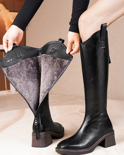 Black knee-high boots with a zipper being pulled open on a beige background