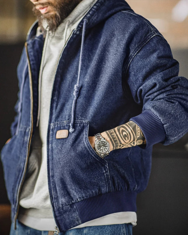 Person wearing a blue denim jacket with a brand logo, standing indoors.
