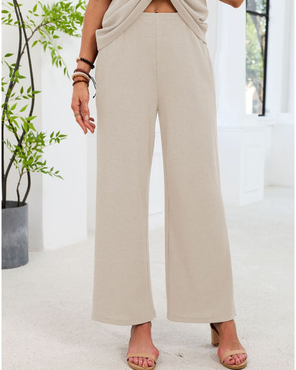 Person wearing beige wide-leg pants standing indoors with a plant in the background