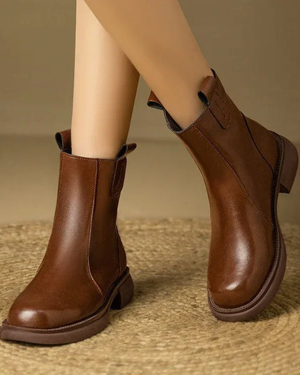 Brown leather ankle boots worn by a person on a textured surface with a neutral background