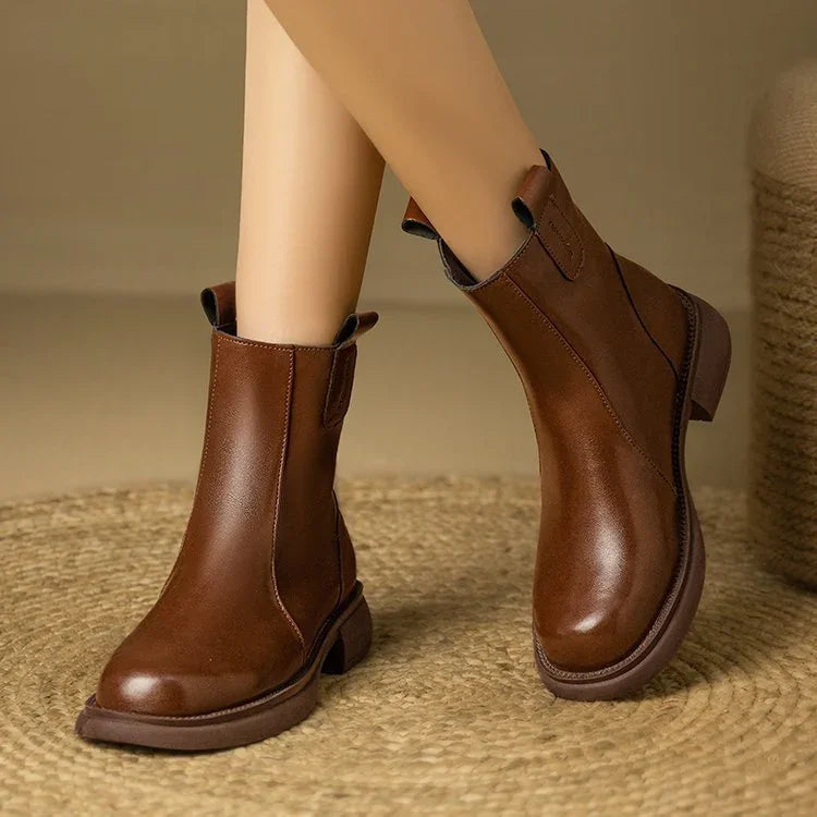 Brown leather ankle boots worn by a person on a textured surface with a neutral background