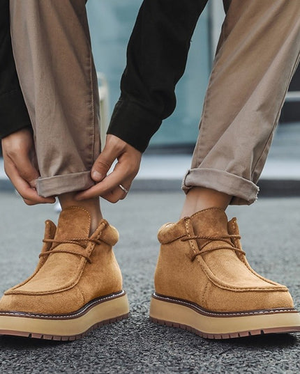 Person wearing tan boots with rolled-up beige pants on a blurred background