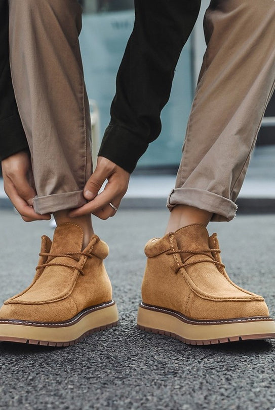 Person wearing tan boots with rolled-up beige pants on a blurred background