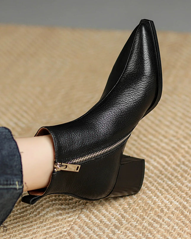 Black leather ankle boot with a gold zipper on a textured surface