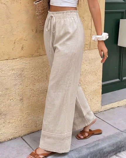 Person wearing beige linen pants and a white top against a stone wall.