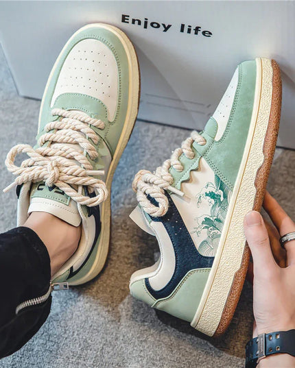 Pair of green and white sneakers with brown soles, held by a hand, on a light gray surface with 'Enjoy life' text in the background.