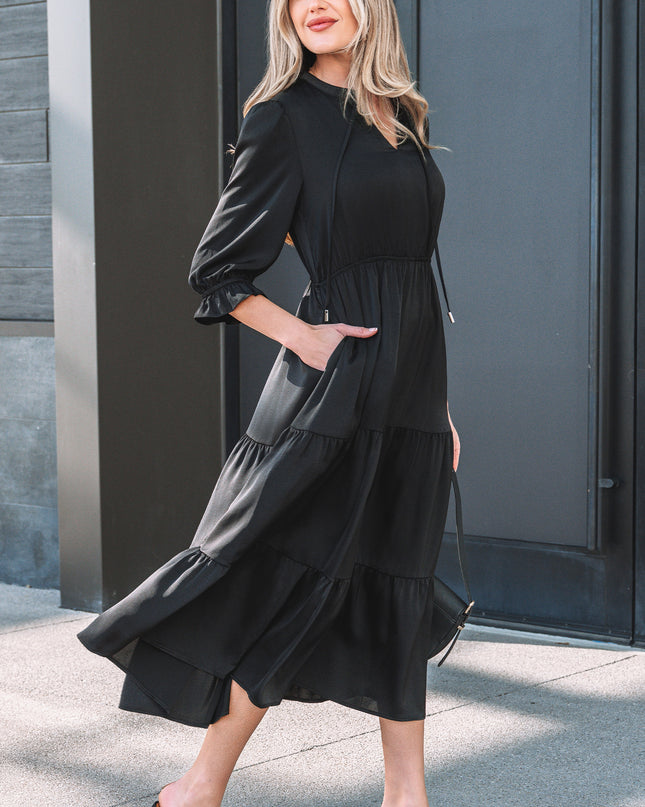 Woman wearing a black dress standing against a gray wall.