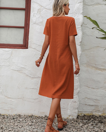 Woman wearing a rust-colored dress standing against a white textured wall.