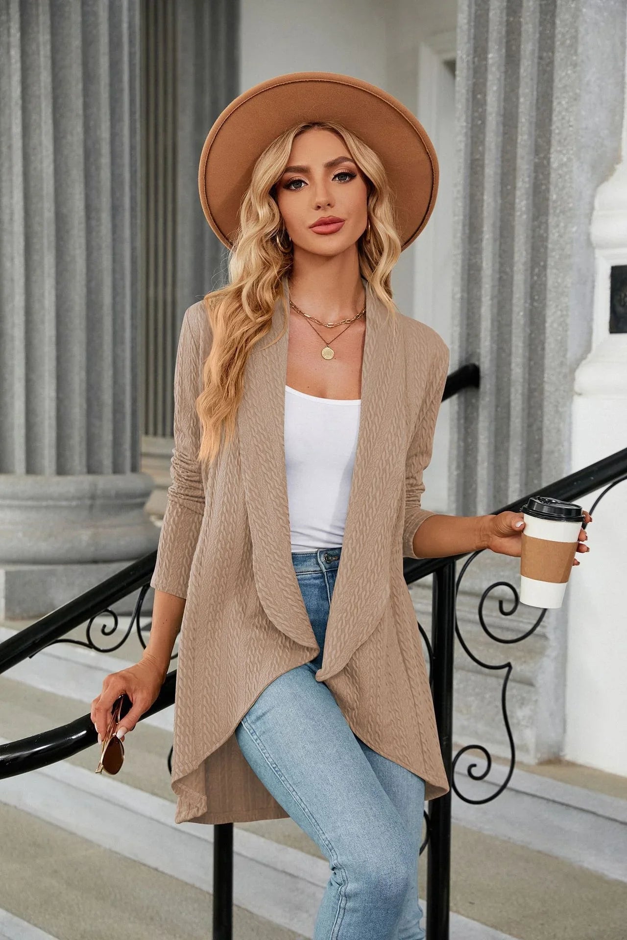 Woman in beige cardigan and hat holding a coffee cup outdoors.