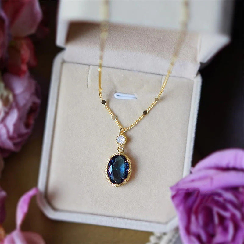 Gold necklace with a blue pendant on a pink cushion, surrounded by pink flowers.