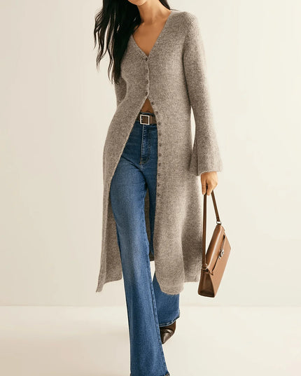 Woman wearing a long gray cardigan, blue jeans, and holding a brown handbag on a beige background