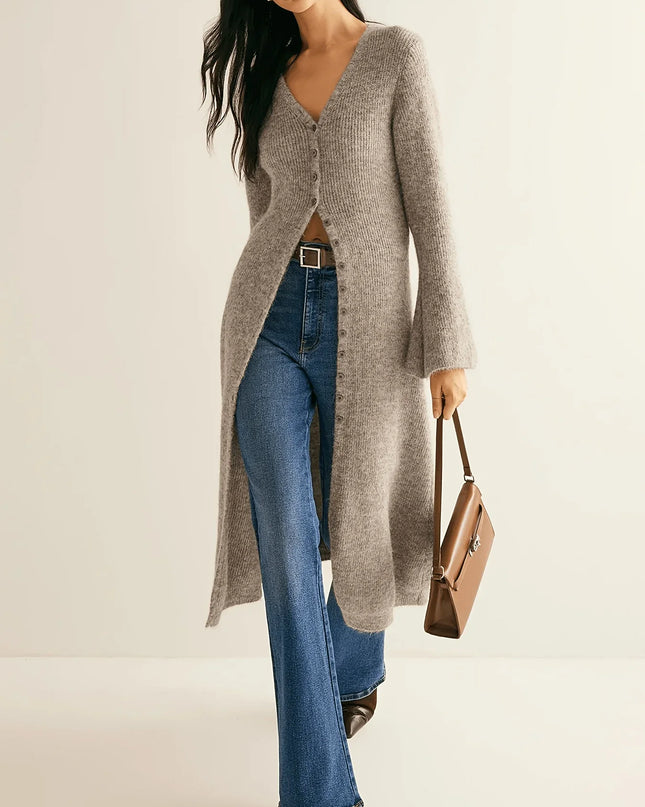 Woman wearing a long gray cardigan, blue jeans, and holding a brown handbag on a beige background