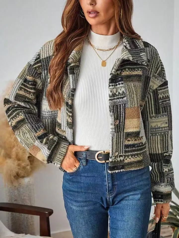 Woman wearing a patterned jacket over a white sweater and blue jeans, standing against a neutral background.