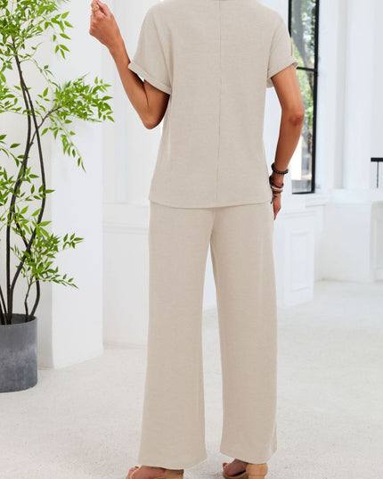 Person wearing a beige outfit standing in a bright room with a plant.