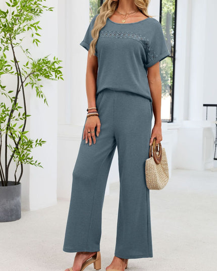 Woman in a blue outfit standing indoors with a plant and chair in the background