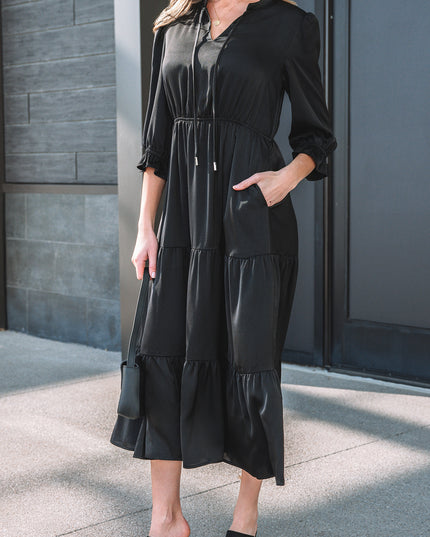 Woman wearing a black dress standing against a gray wall.