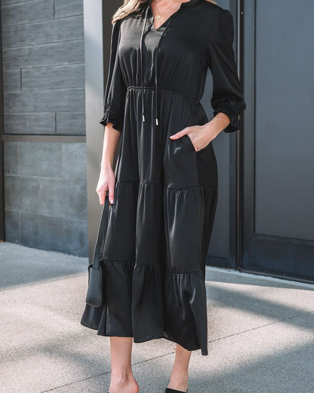Woman wearing a black dress standing against a gray wall.