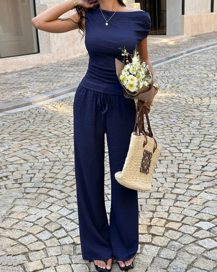 Woman in a navy blue outfit holding flowers and a straw bag on a cobblestone street.