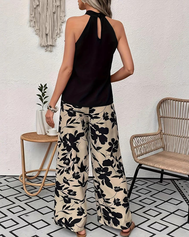 Woman wearing a black halter top and floral pants in a room with a chair and plant.