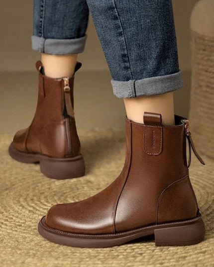 Brown leather boots worn with rolled-up jeans on a textured surface