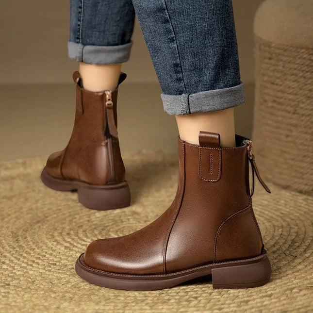 Brown leather boots worn with rolled-up jeans on a textured surface