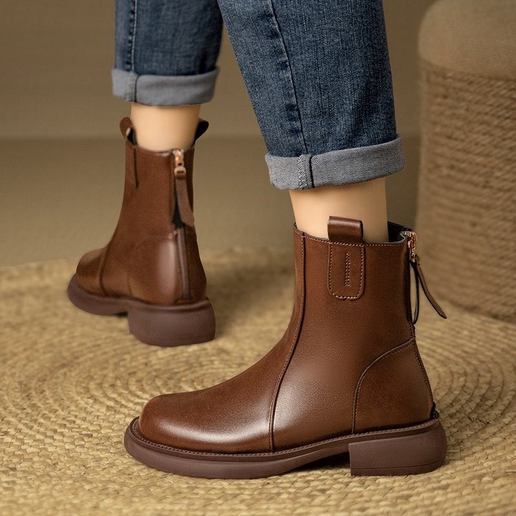 Brown leather boots worn with rolled-up jeans on a textured surface