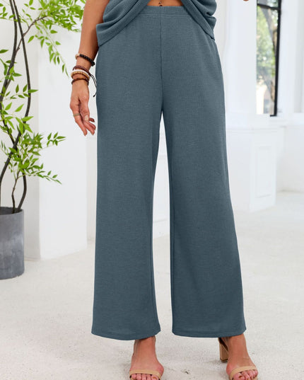 Person wearing teal wide-leg pants standing indoors with a plant in the background