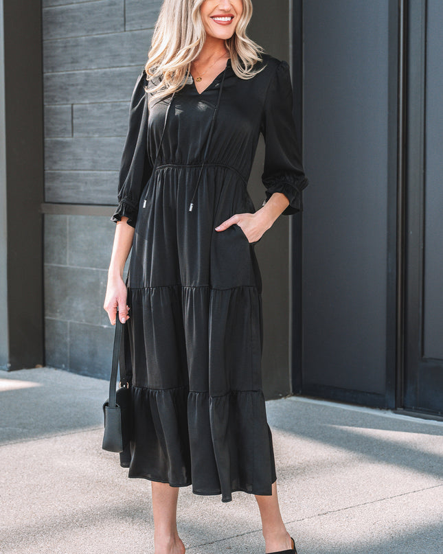 Woman wearing a black dress standing against a gray wall.