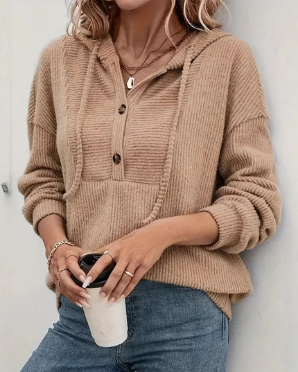 Person wearing a beige ribbed sweater holding a coffee cup against a white wall