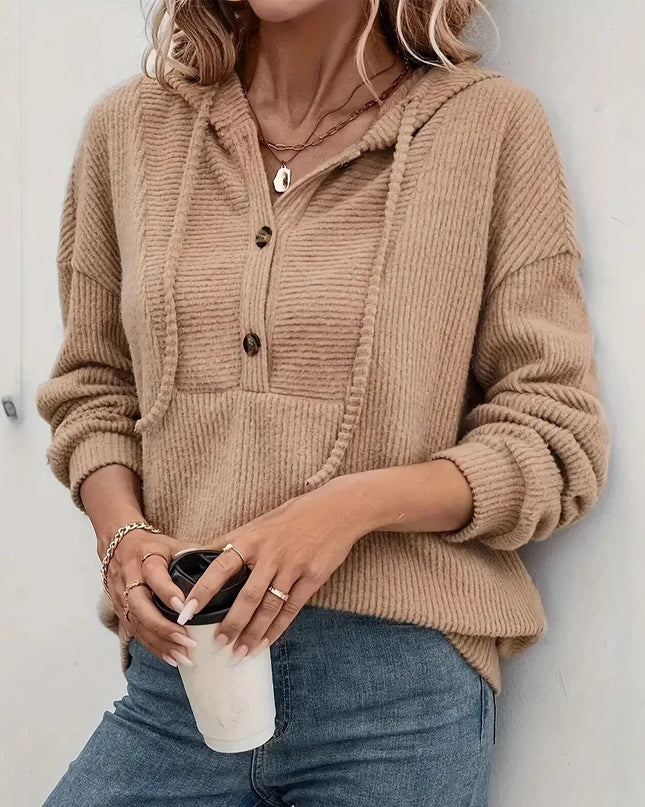 Person wearing a beige ribbed sweater holding a coffee cup against a white wall
