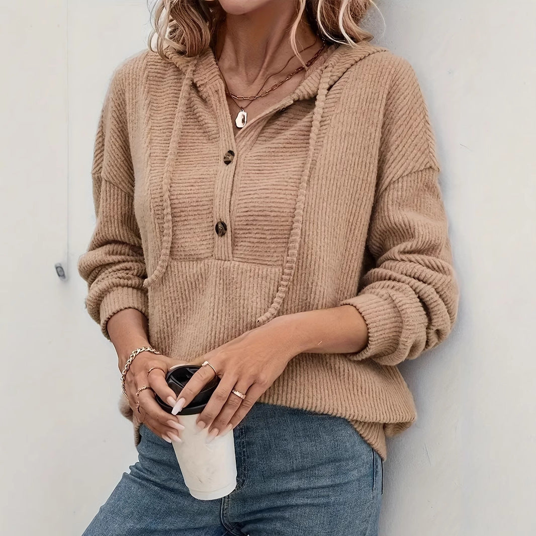 Person wearing a beige ribbed sweater holding a coffee cup against a white wall