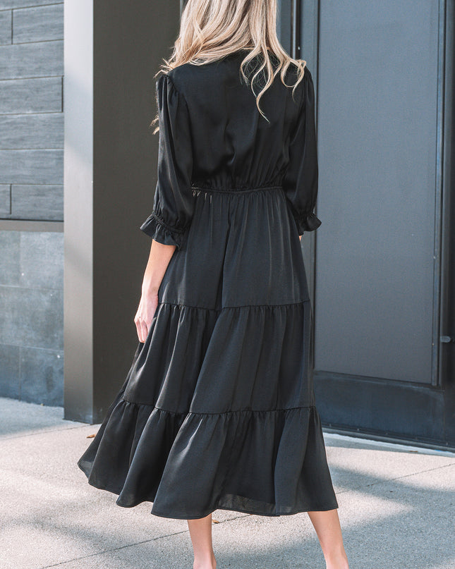 Woman wearing a black dress standing in front of a gray door.