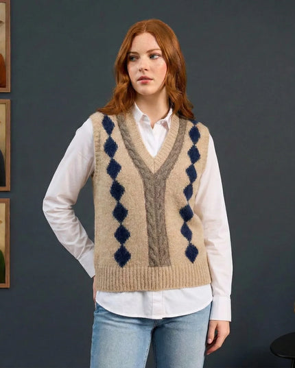 Woman wearing a patterned sweater vest with framed animal portraits on a dark wall.