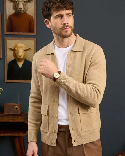 Man wearing a beige cardigan in a room with framed animal portraits on the wall.