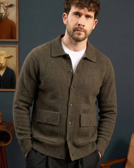 Man wearing a brown cardigan standing against a blue wall with framed pictures of sheep.